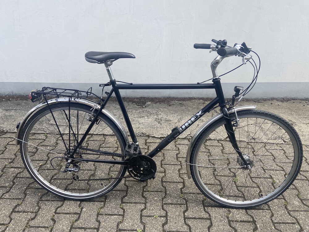 Schwarzes Trekkingfahrrad mit Gepäckträger, Schutzblechen und Scheinwerfer steht auf gepflastertem Boden.
Verkauf gebrauchter Fahrräder Aachen